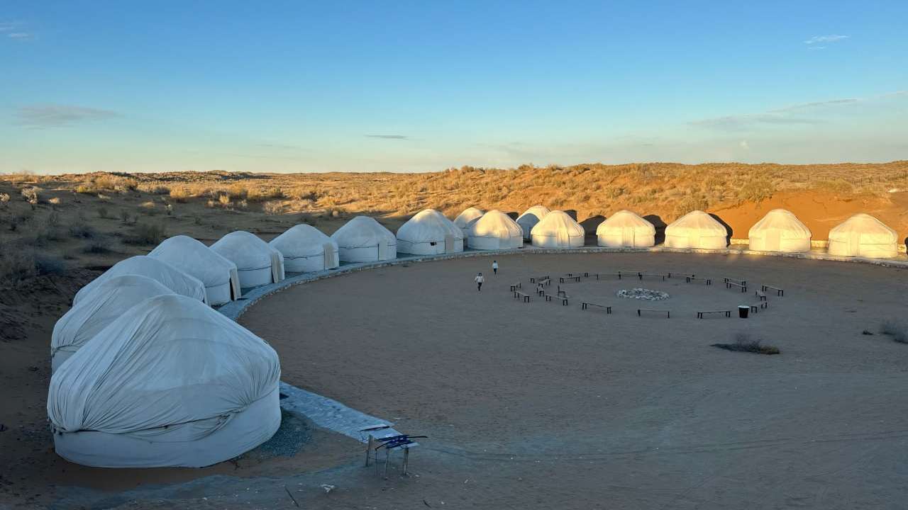 The yurts of Sputnik Navoi in low golden evening light, seen across the open sand