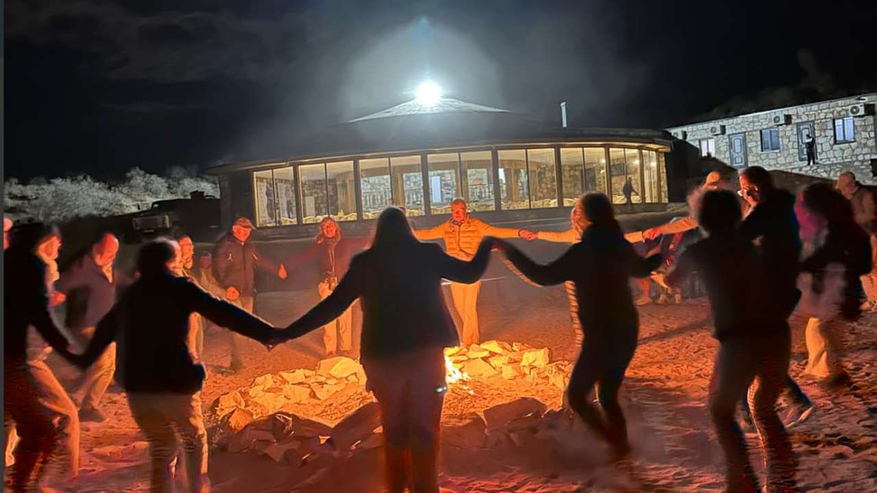 Guests dancing hand in hand around the campfire after dark