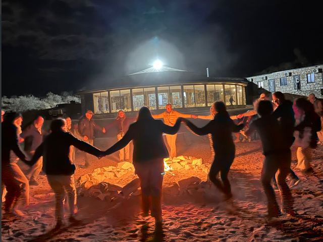 Guests dancing hand in hand around the campfire after dark