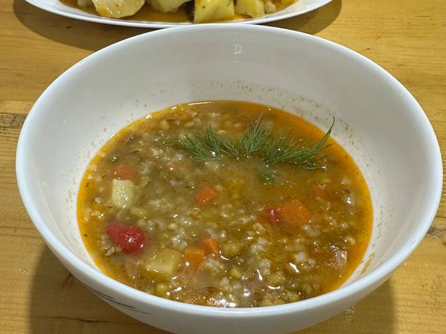 A bowl of soup with potatoes and vegetables on a wooden table