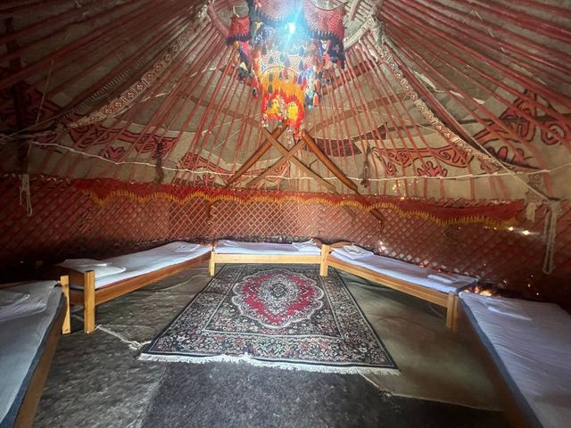 The felt-lined interior of a yurt with beds and a red carpet