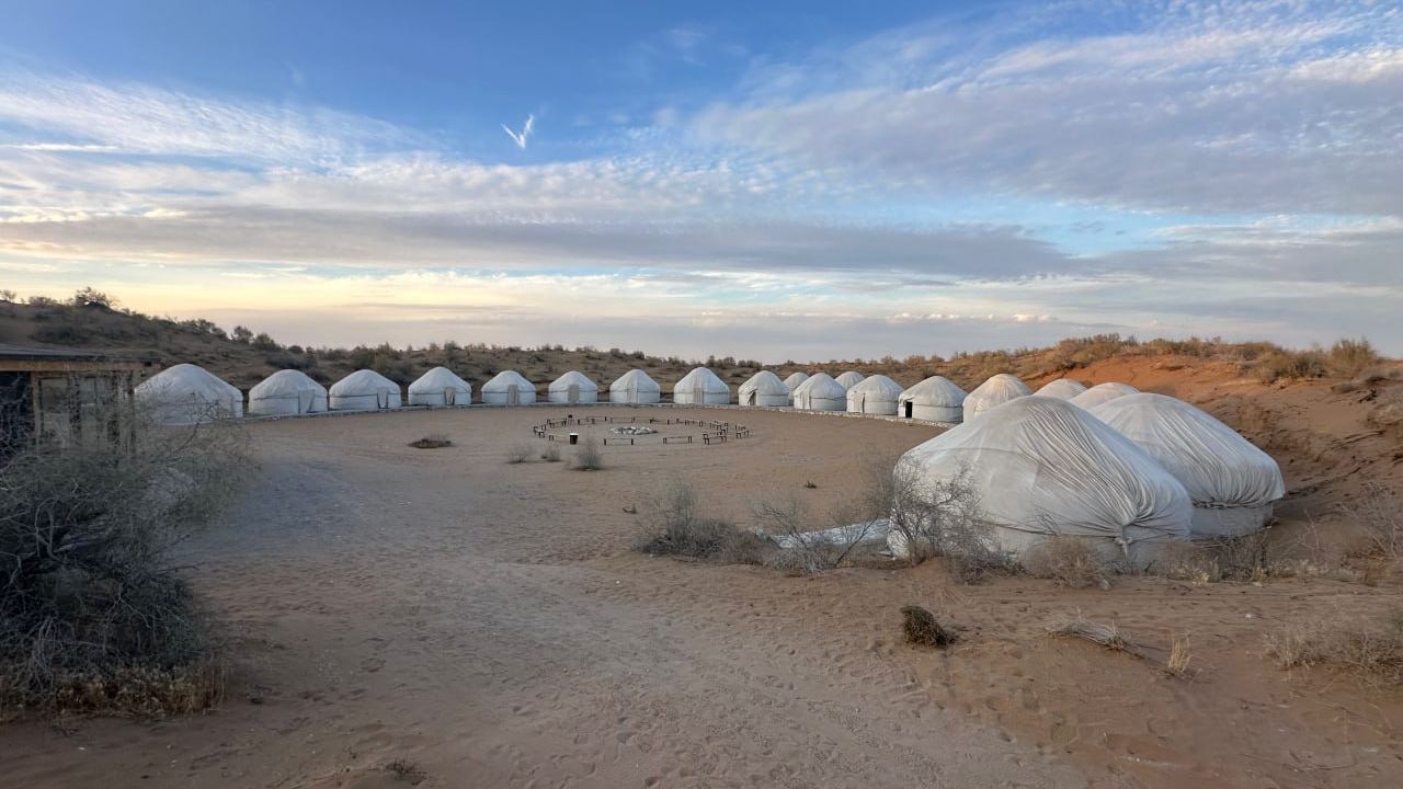 Yurts of Sputnik Navoi camp curving around an open sand clearing in the Kyzylkum desert at dusk